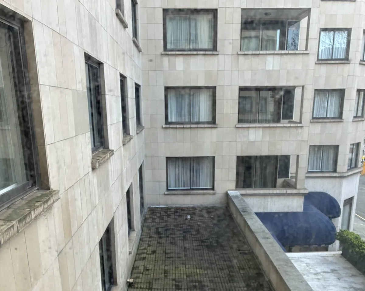 Internal courtyard elevation showing tired stone facing and a stained flat roof.